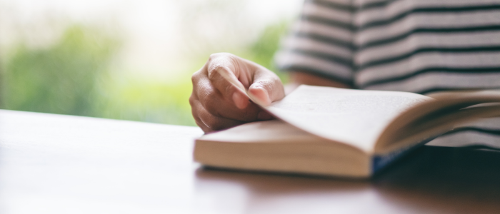 The image is cropped, showing only a hand resting on the pages of a book, suggesting that the person is reading.