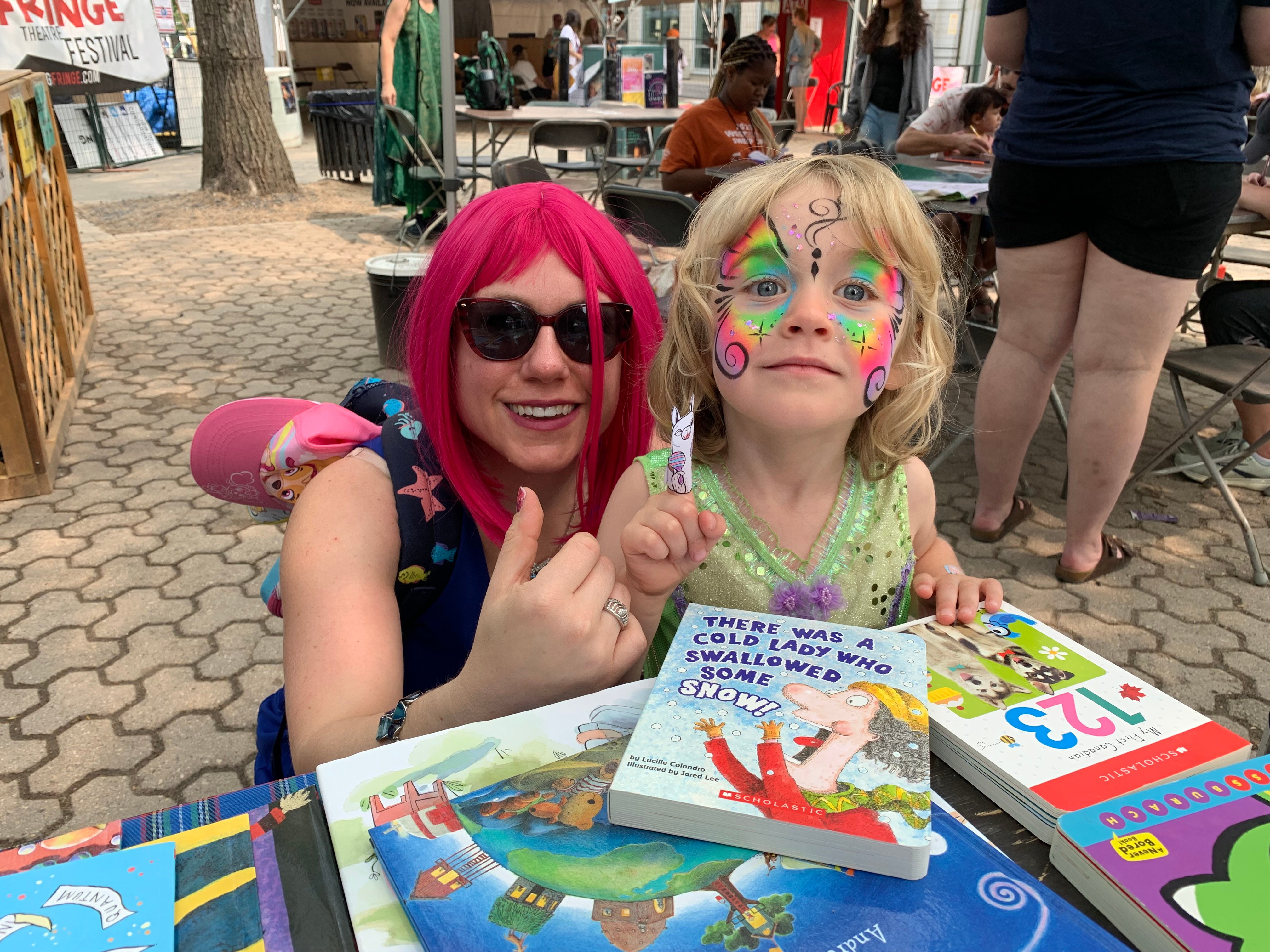 A kid and a lady with a pink wig in front of books